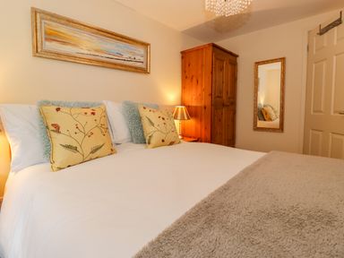 A bedroom with a bed with yellow floral pillows a wooden wardrobe a mirror and a painting at Maple Cottage in Keswick