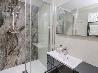 A bathroom with a glass shower enclosure and a sink with a mirror above at Maple Cottage in Keswick