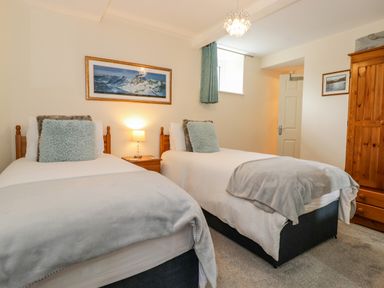 A bedroom with two single beds a bedside table with lamp a wooden wardrobe and framed pictures at Maple Cottage in Keswick