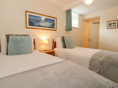 A bedroom with two single beds a bedside table with a lamp and framed pictures on the walls at Maple Cottage in Keswick