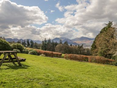 A grassy garden with a wooden picnic bench and hedges overlooking distant hills and trees at Garden Cottage in Keswick