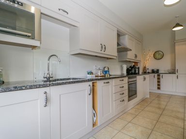 A kitchen with white cabinets granite countertops a sink an oven microwave and wall clock at Garden Cottage in Keswick
