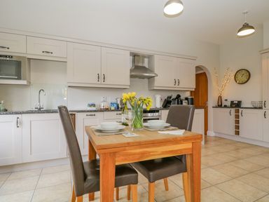 A kitchen with white cabinets a wooden table set for two with a vase of yellow flowers and two brown chairs at Garden Cottage in Keswick