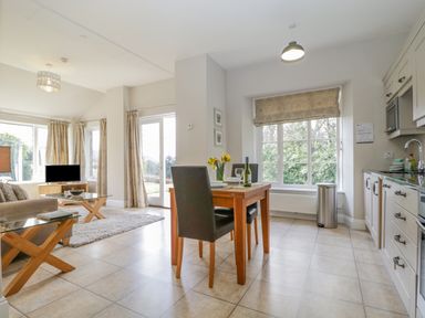 A kitchen and dining area with a wooden table and two chairs near a window and a living room with a sofa and a TV at Garden Cottage in Keswick