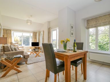 A dining area with a wooden table set for two and a living room with a sofa and armchairs at Garden Cottage in Keswick