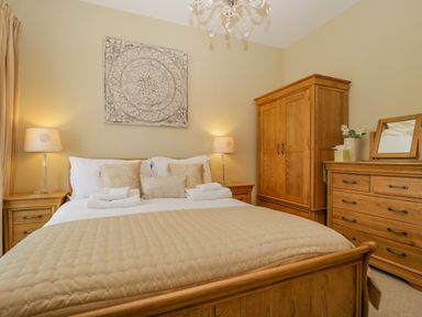 A bedroom with a wooden bed and beige bedding two bedside tables with lamps wooden wardrobe and dresser with mirror at Garden Cottage in Keswick