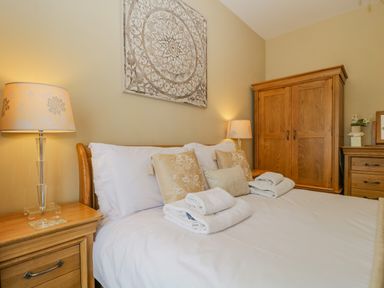 A bedroom with a double bed white linens wooden bedside tables lamps a wooden wardrobe and decorative pillows at Garden Cottage in Keswick