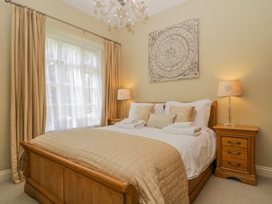 A bedroom with a wooden bed beige bedding bedside tables with lamps and a window with curtains at Garden Cottage in Keswick