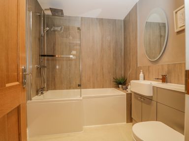A bathroom with a bathtub and shower, sink with mirror, and toilet at Garden Cottage in Keswick