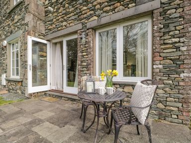 A stone exterior patio with a metal table and two chairs with cushions and flowers on the table at Garden Cottage in Keswick