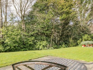 A garden with green grass trees and shrubs and a metal round table in the foreground at Garden Cottage in Keswick