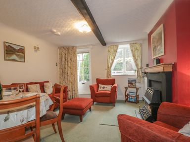 A living room with red armchairs and ottoman near a fireplace with paintings on walls at Derwent Edge in Portinscale