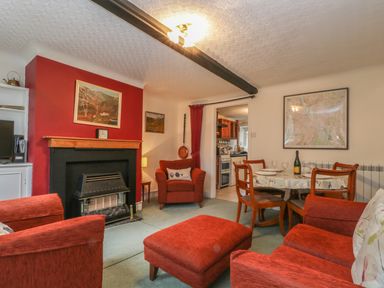 A living room with red armchairs a fireplace a dining table and kitchen in the background at Derwent Edge in Portinscale