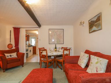 A sitting room with red chairs a dining table and a view into the kitchen at Derwent Edge in Portinscale