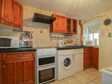 A kitchen with wooden cabinets a stove microwave toaster washing machine and dishwasher at Derwent Edge in Portinscale
