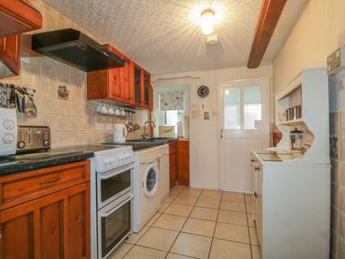 A kitchen with wooden cabinets a white oven a washing machine and a white cupboard at Derwent Edge in Portinscale