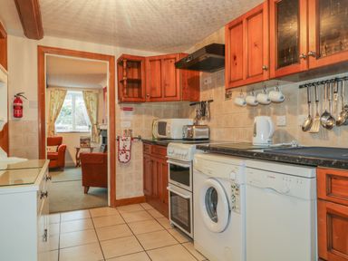A kitchen with wooden cabinets white appliances and a view into a sitting room at Derwent Edge in Portinscale