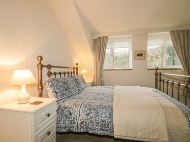 A bedroom with a metal bed frame patterned bedding bedside tables with lamps and windows with curtains at Derwent Edge in Portinscale