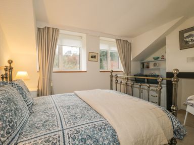A bedroom with a metal bed frame blue patterned bedding bedside lamp and windows at Derwent Edge in Portinscale