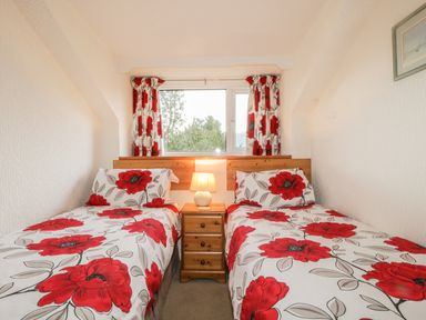 A small bedroom with two single beds with floral bedding and a nightstand with a lamp between them at Derwent Edge in Portinscale