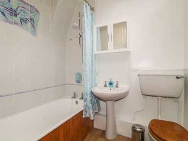 A bathroom with a bathtub, shower curtain, pedestal sink, wall-mounted mirror cabinet, and toilet with a wooden seat at Derwent Edge in Portinscale