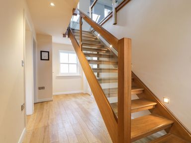 A wooden staircase with glass panels along one side in a hallway with wooden flooring and a window at Wrenville in Keswick