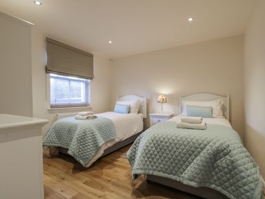 A bedroom with two single beds with blue quilts bedside table with lamp and folded towels on beds at Wrenville in Keswick