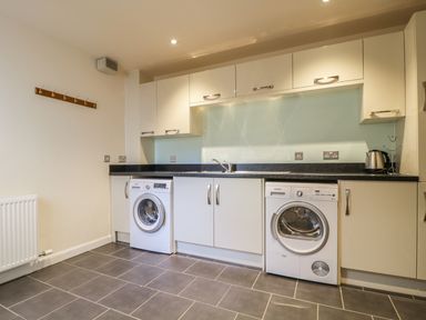 A laundry room with washing machine dryer cabinets and a kettle on the counter at Wrenville in Keswick