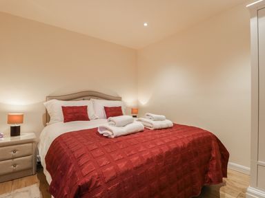 A bedroom with a bed with red bedding and two bedside tables with lamps at Wrenville in Keswick