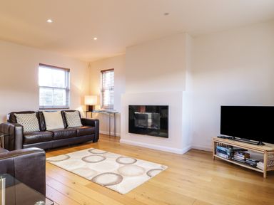 A living room with a brown leather sofa a rug a wall-mounted fireplace and a TV on a wooden stand at Wrenville in Keswick
