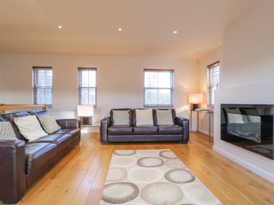 A living room with two brown leather sofas a patterned rug wooden floor and windows at Wrenville in Keswick
