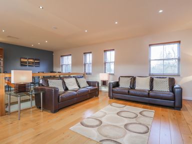 A living room with two brown leather sofas pillows a patterned rug and lamps on glass tables at Wrenville Keswick