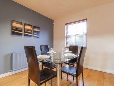 A dining room with a glass table set for four and dark chairs near a window at Wrenville in Keswick