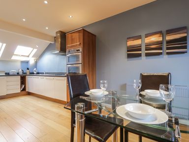 A kitchen with white cabinets and a glass dining table set with plates and glasses at Wrenville in Keswick