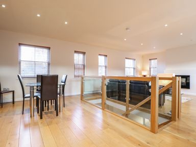 A dining area with a glass table and chairs near windows and a living space with sofas separated by glass railings at Wrenville in Keswick