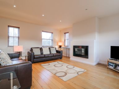 A living room with two brown leather sofas a patterned rug a wall-mounted fireplace and a television on a wooden stand at Wrenville in Keswick