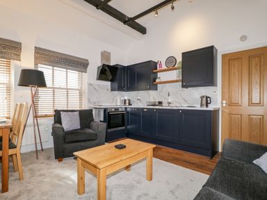 A living room with a wooden coffee table two armchairs carpet and a kitchen with black cabinets and marble backsplash at The Old Hayloft in Keswick