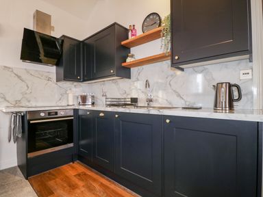 A kitchen with black cabinets marble backsplash wooden shelves and stainless steel appliances at The Old Hayloft in Keswick