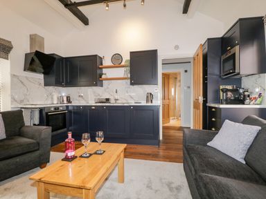 A kitchen and living area with black cabinets wooden coffee table grey sofas and a clock on the wall at The Old Hayloft in Keswick