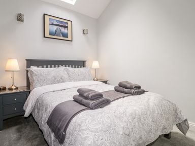 A bedroom with a double bed grey headboard bedside tables with lamps and folded towels on bed at The Old Hayloft in Keswick