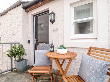 A small outdoor seating area with wooden table and chairs by a black door and window at The Old Hayloft in Keswick