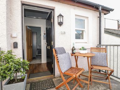 An outdoor seating area with a wooden table and two chairs with cushions and a plant near an open door at The Old Hayloft in Keswick