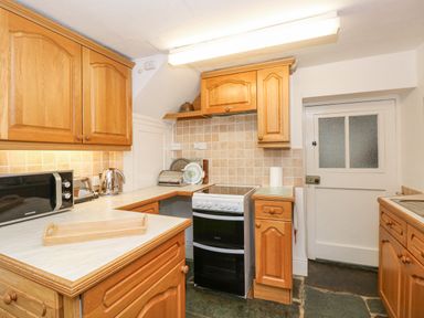 A kitchen with wooden cabinets a microwave kettle stove and a wooden tray on the counter at Prospect Lodge in Portinscale