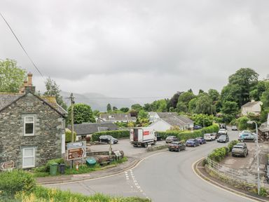 A roadside view of multiple cars parked near stone and white houses with green trees in the background at Prospect Lodge in Portinscale