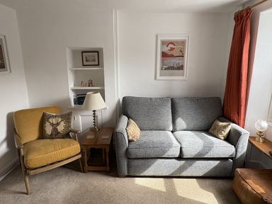 A living room with a sofa, armchair, lamp, and bookshelf at Prospect Lodge in Portinscale