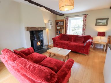 A living room with two red sofas a wood burning stove and a wooden coffee table at Mell View Cottage in Ullswater