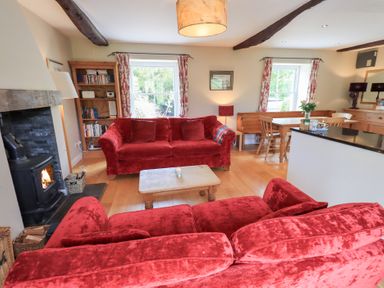 A living room with red sofas wooden coffee table bookshelf and wood burning stove at Mell View Cottage in Ullswater