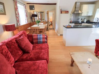 A living room with a red sofa wooden dining table and a kitchen area at Mell View Cottage in Ullswater