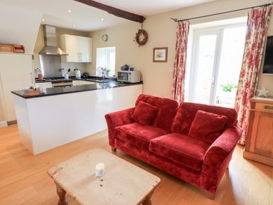 A red sofa and wooden table in a living room next to a kitchen with white cabinets at Mell View Cottage in Ullswater