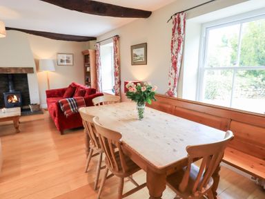 A dining area with wooden table and chairs a red sofa and a wood burning stove in a living room at Mell View Cottage Ullswater